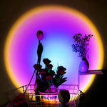 Decorative setup with flowers, a vase, and a lamp against a colorful circular light projection.