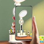 Hand holding a smartphone displaying an image of a desk setup with a lamp and stationery items.