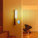 Wall-mounted light fixture with sensor icon in a room with wooden floor and chair.
