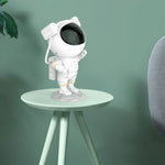 White astronaut figurine on a small round table against a green background