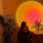 Person sitting in a chair with a large circular light source casting a warm glow, surrounded by plants.