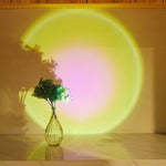 Vase with greenery on a table with a colorful circular light projection on the wall.