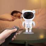 Person holding a remote control next to an astronaut figurine on a table with a blurred background of a person sleeping.