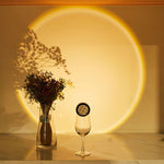 Vase with flowers and a wine glass on a reflective surface with a circular light projection on the wall.
