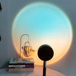 Lamp projecting a rainbow pattern on a wall with books and a small sculpture in the foreground.