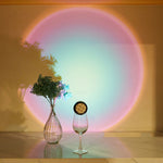 Vase with flowers and a glass on a reflective surface with a colorful circular light projection on the wall.