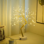 Decorative LED tree on a table with a cup and saucer in a softly lit room.